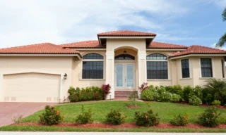beige house with a light red roofing and a patio on the front